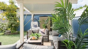 Un patio techado con muebles de mimbre, una mecedora colgante y plantas en macetas.