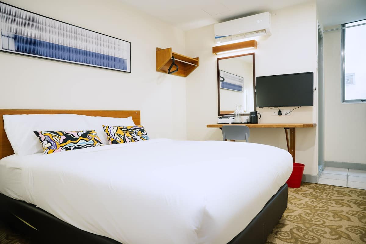 A hotel room with a large bed, a desk with a mirror, a television, and a wall-mounted air conditioning unit.
