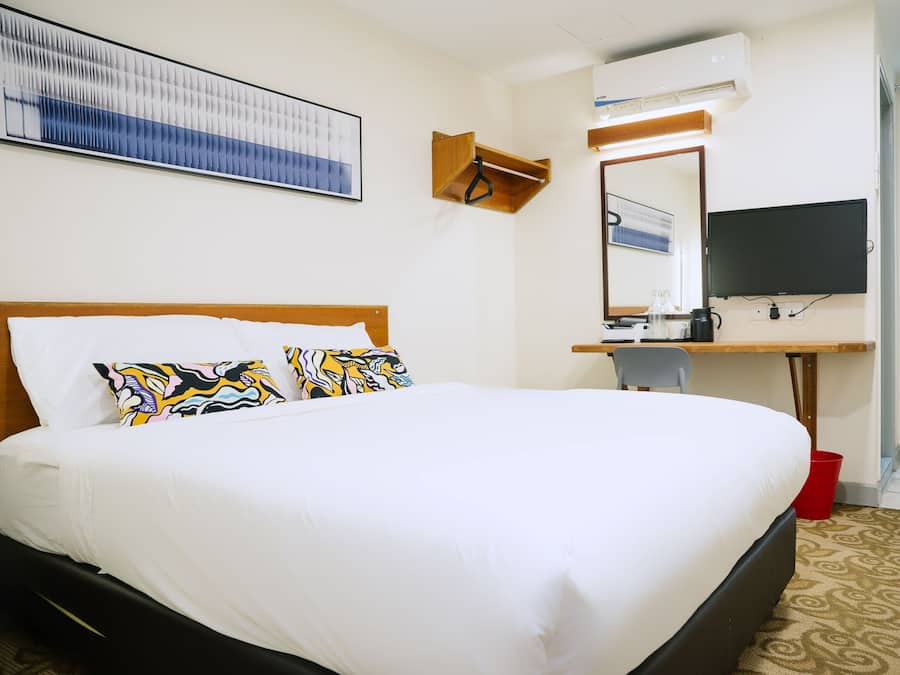 A hotel room with a large bed, a desk with a mirror, a television, and a wall-mounted air conditioning unit.