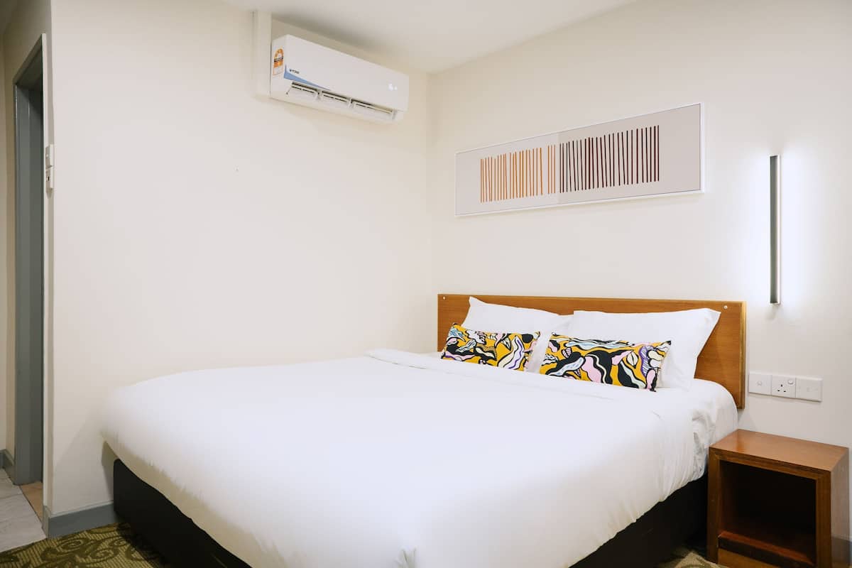 A neatly made bed with white bedding, a wooden headboard, and a colorful pillow. There is a small wooden nightstand beside the bed.
