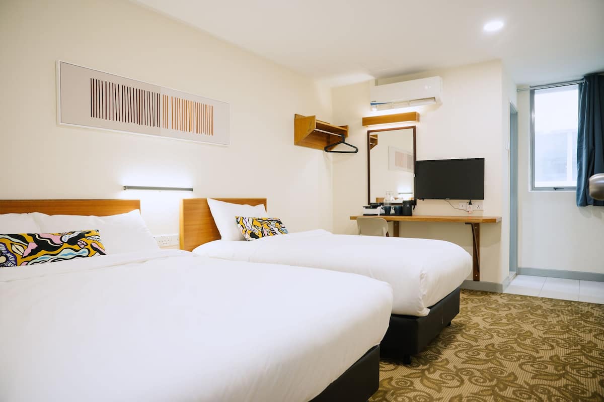 A hotel room with two beds, a desk with a computer, a TV, and a window with curtains.