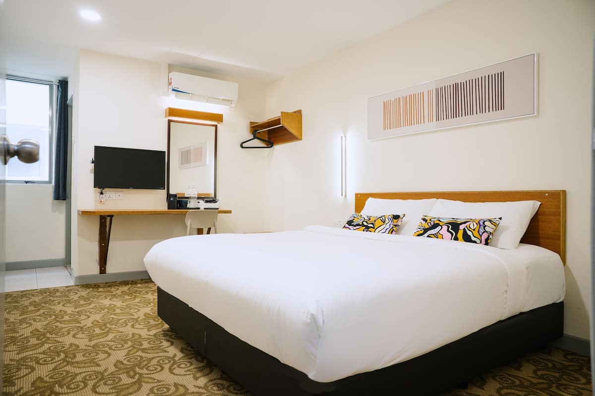 A hotel room with a large bed, a desk with a chair, a flat-screen TV, and a mirror.
