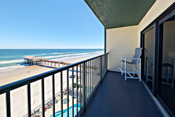 A balcony with a view of the beach and ocean, a pool, and two striped chairs. - True Oceanfront 1BR | 7th-Floor Balcony | Heated Pool + Hot Tub | Free Daily Activities Included! (Daytona Beach Shores)