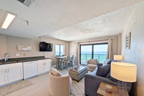 A modern living room with a sofa, a coffee table, and a TV. There is a dining area with a table and chairs. The room has a view of the ocean. - True Oceanfront 1BR | 7th-Floor Balcony | Heated Pool + Hot Tub | Free Daily Activities Included! (Daytona Beach Shores)