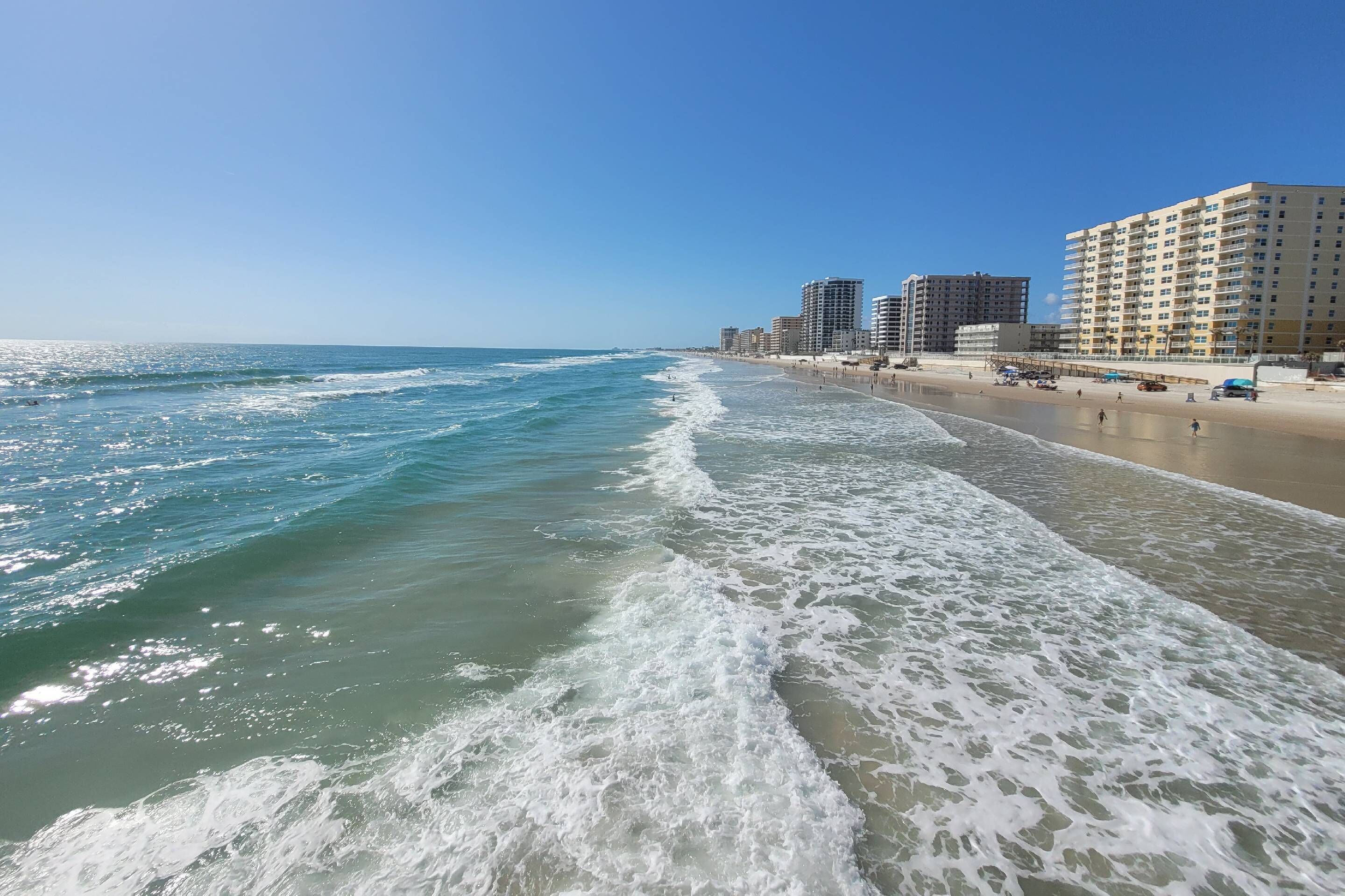 A beach with ocean waves, a sandy shore, and high-rise buildings in the background.
