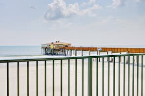 A beach with a wooden pier extending into the ocean, a building on the pier, and a clear sky.