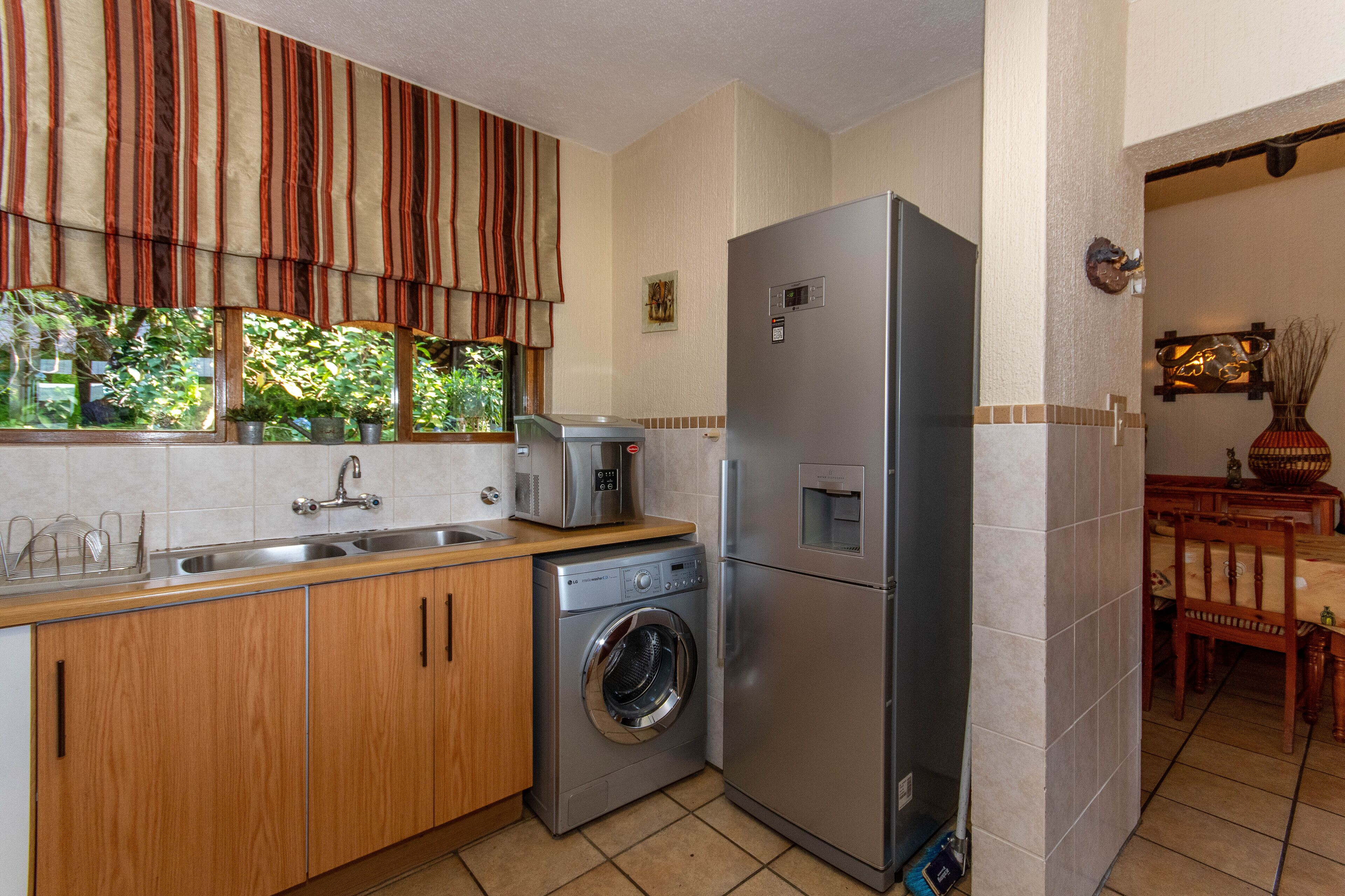 Una cuina amb armaris de fusta, un refrigerador d'acer inoxidable, una rentadora i una finestra amb cortines.
