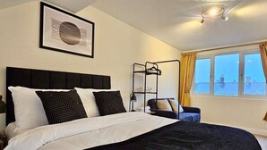 Une chambre à coucher comprenant un lit, une table de chevet, un portant à vêtements et une fenêtre avec des rideaux.