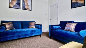 Une pièce avec deux canapés bleus, une porte et deux tableaux abstraits accrochés au mur.