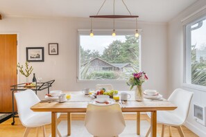 A dining area with a wooden table, white chairs, and a view of a house through a large window.