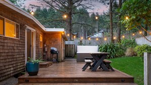 A wooden deck with a table and chairs, surrounded by a wooden fence and greenery. - Four Bears by AvantStay | Walk to Beach, Hot Tub, Ocean View (Arch Cape)