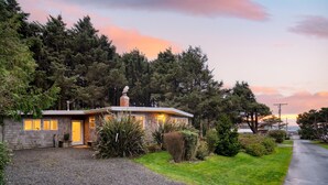 A single-story house with a gravel driveway, surrounded by dense trees and a clear sky. - Four Bears by AvantStay | Walk to Beach, Hot Tub, Ocean View (Arch Cape)