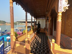 A room with a balcony overlooking a body of water, featuring ornate wooden furniture and a patterned floor. - Goona palace houseboats  (Srinagar)
