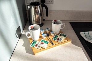 A kitchen counter with a coffee maker, two white mugs, and packets of tea and milk. - Sleek 3-BR Apartment, Central Hartlepool (Hartlepool)