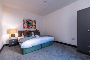 A bedroom with a bed, a nightstand, a lamp, a wardrobe, and a colorful abstract painting on the wall. - Sleek 3-BR Apartment, Central Hartlepool (Hartlepool)