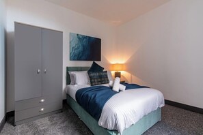 A bedroom with a bed, a wardrobe, a wall-mounted artwork, and a bedside lamp. - Stylish 3-BR Apartment in Hartlepool (Hartlepool)