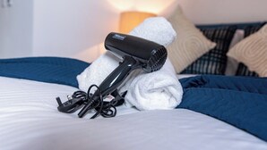 Un secador de pelo sobre una cama con una toalla blanca, una manta azul y una almohada.