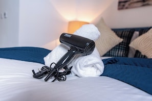 A hair dryer on a bed with a white towel, a blue blanket, and a pillow. - Stylish 3-BR Apartment in Hartlepool (Hartlepool)