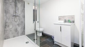 Un baño moderno con ducha envuelta en vidrio, inodoro blanco y lavamanos blanco con un espejo encima.