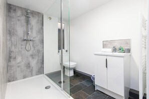 A modern bathroom with a glass-enclosed shower, a white toilet, and a white sink with a mirror above it. - Stylish 3-BR Apartment in Hartlepool (Hartlepool)
