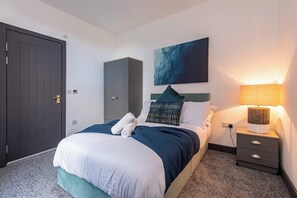 A hotel room with a bed, a wardrobe, a painting on the wall, a nightstand, and a lamp. - Stylish 3-BR Apartment in Hartlepool (Hartlepool)