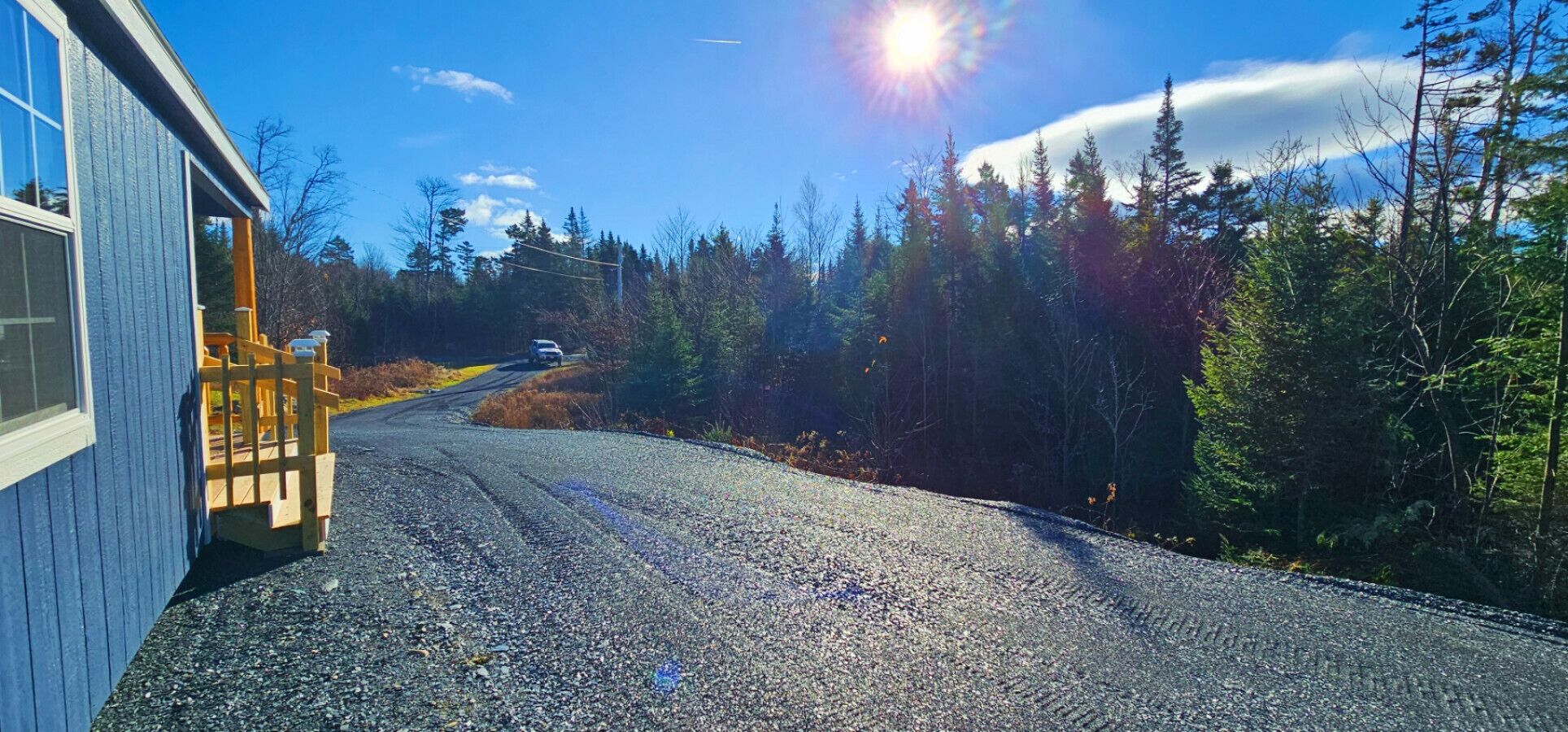 A gravel road leading to a wooden deck with a house on the left.