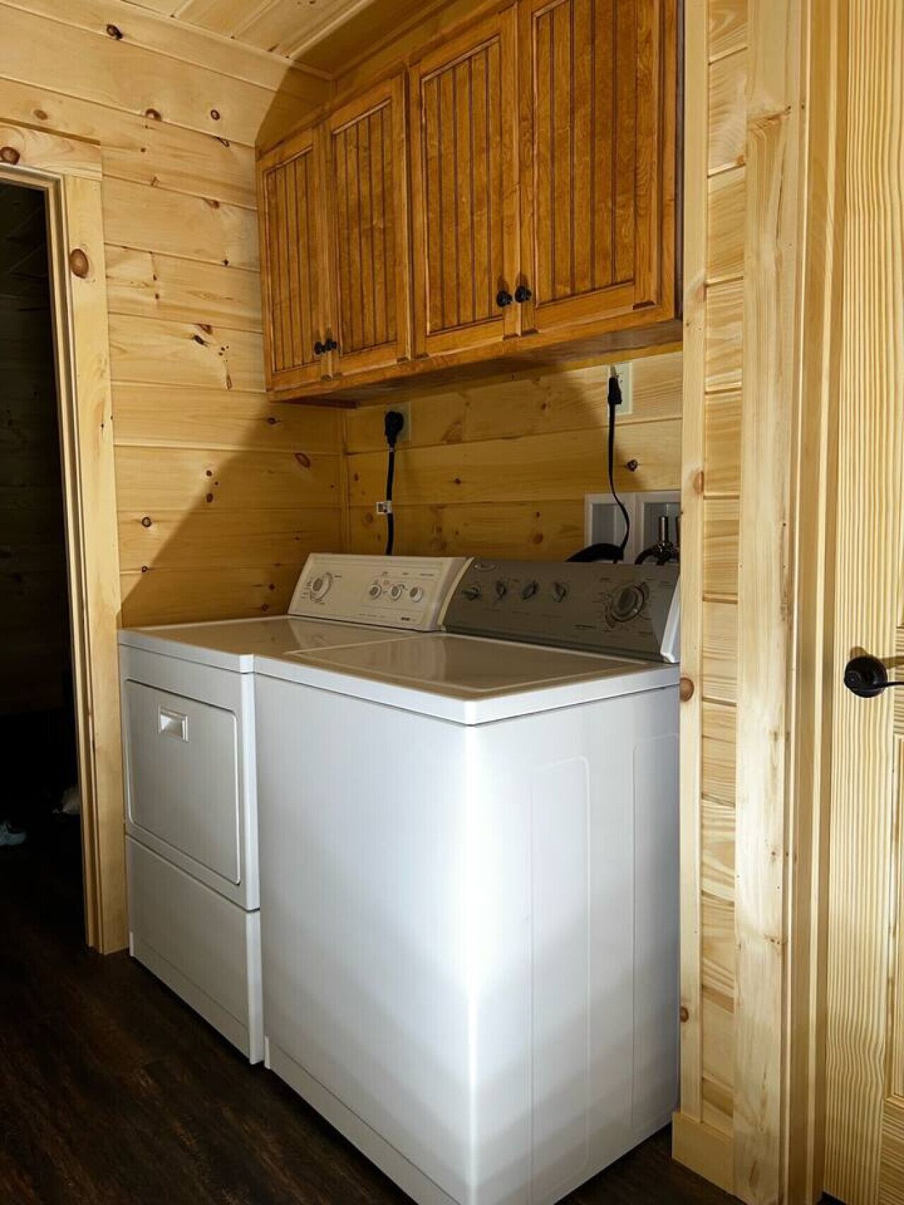 A compact laundry room with wooden walls and cabinets, a washing machine, and a dryer.