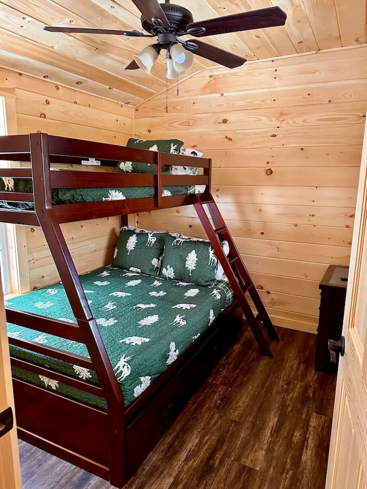 Un letto a castello con struttura in legno e biancheria verde, una ventola a soffitto e pareti in legno.