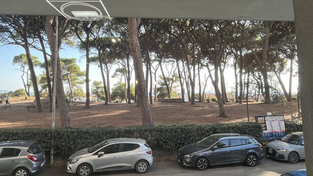 Un'area di parcheggio con diverse auto, alberi e un cartello sullo sfondo.