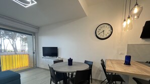 Un soggiorno moderno con zona pranzo, televisione a schermo piatto, orologio e una grande finestra vista alberi.