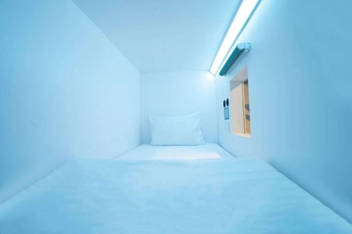 A small, white, narrow room with a single bed and a skylight.