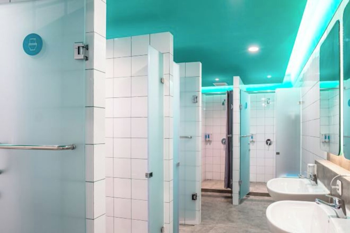 A modern bathroom with white tiles, a glass partition, and a teal ceiling.