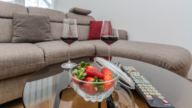 A glass bowl of strawberries on a table with two wine glasses and a remote control. - Holiday home Loncar (Vir)