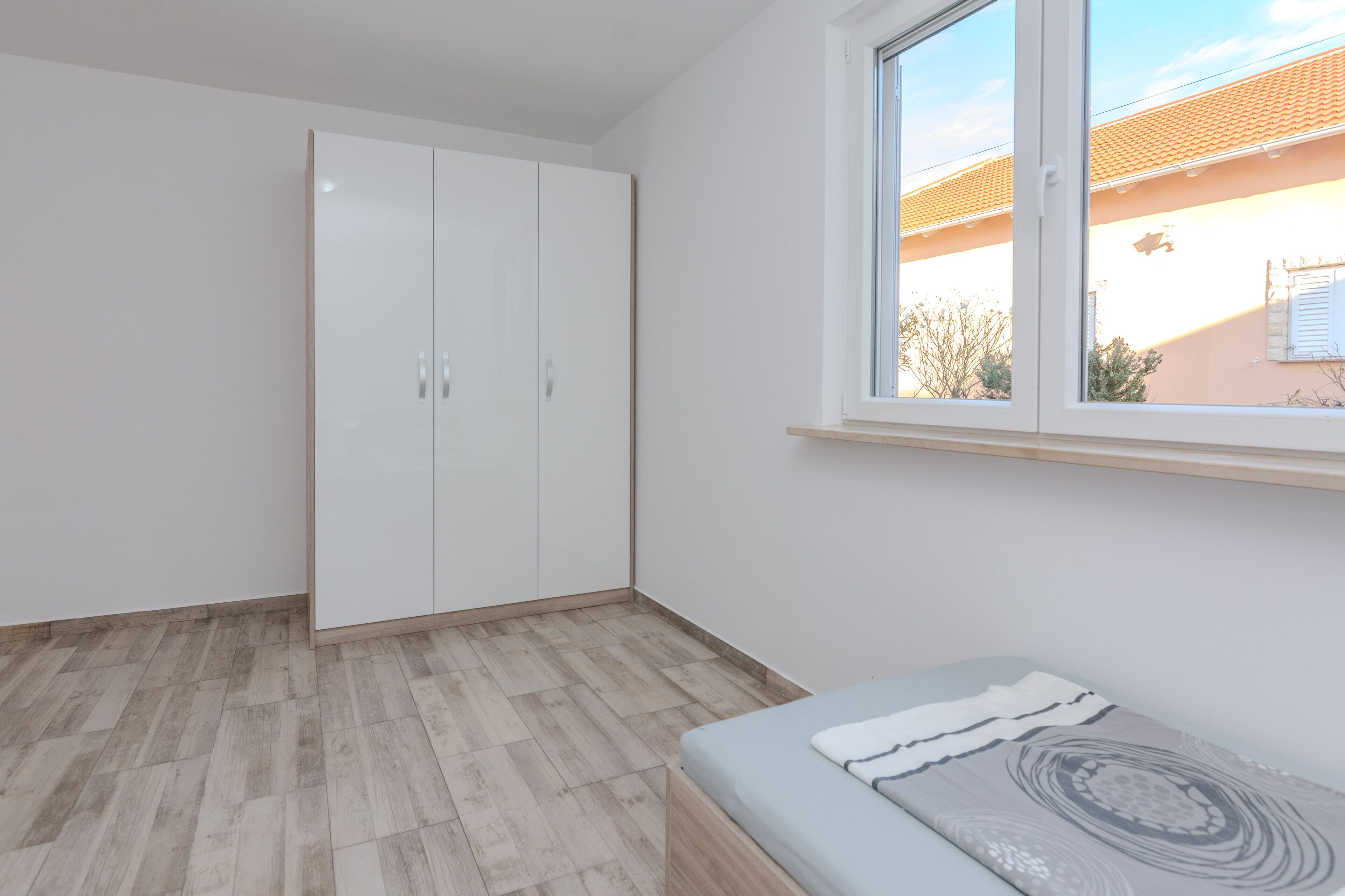 Quarto com cama, guarda-roupa e janela com vista para uma casa.