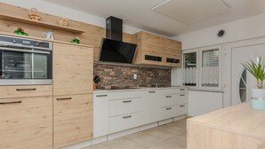 A modern kitchen with wooden cabinets, a built-in oven, and a stone backsplash. - Holiday home Loncar (Vir)
