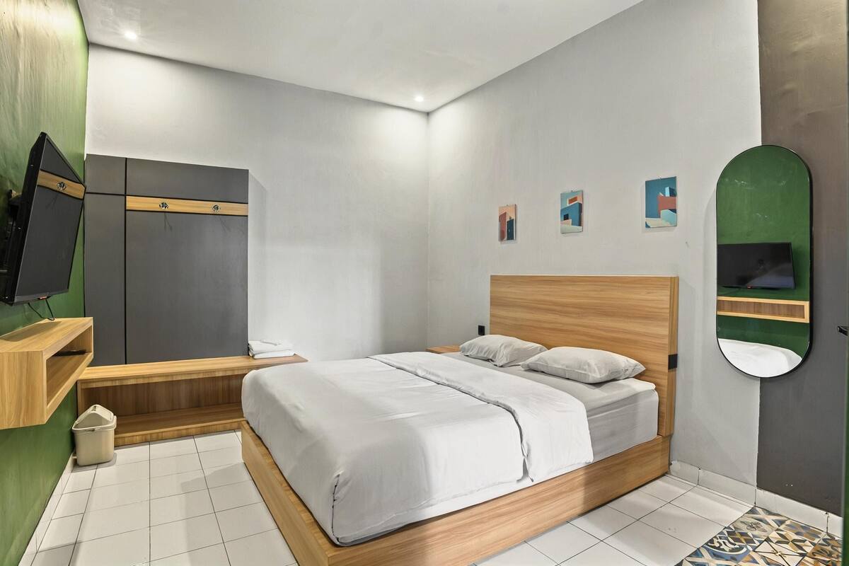 A modern bedroom with a bed, a wooden bench, a TV, and a mirror.