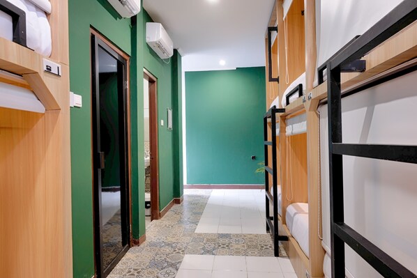 A corridor with bunk beds, a green wall, and a tiled floor.