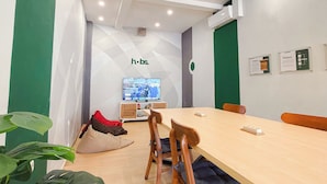 A conference room with a long table, chairs, a television, and a logo on the wall. - HUBS Hostel Yogyakarta (Yogyakarta)