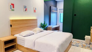 A modern hotel room with a wooden headboard, a bed with white linens, a bedside table, a green wall, and a window. - HUBS Hostel Yogyakarta (Yogyakarta)