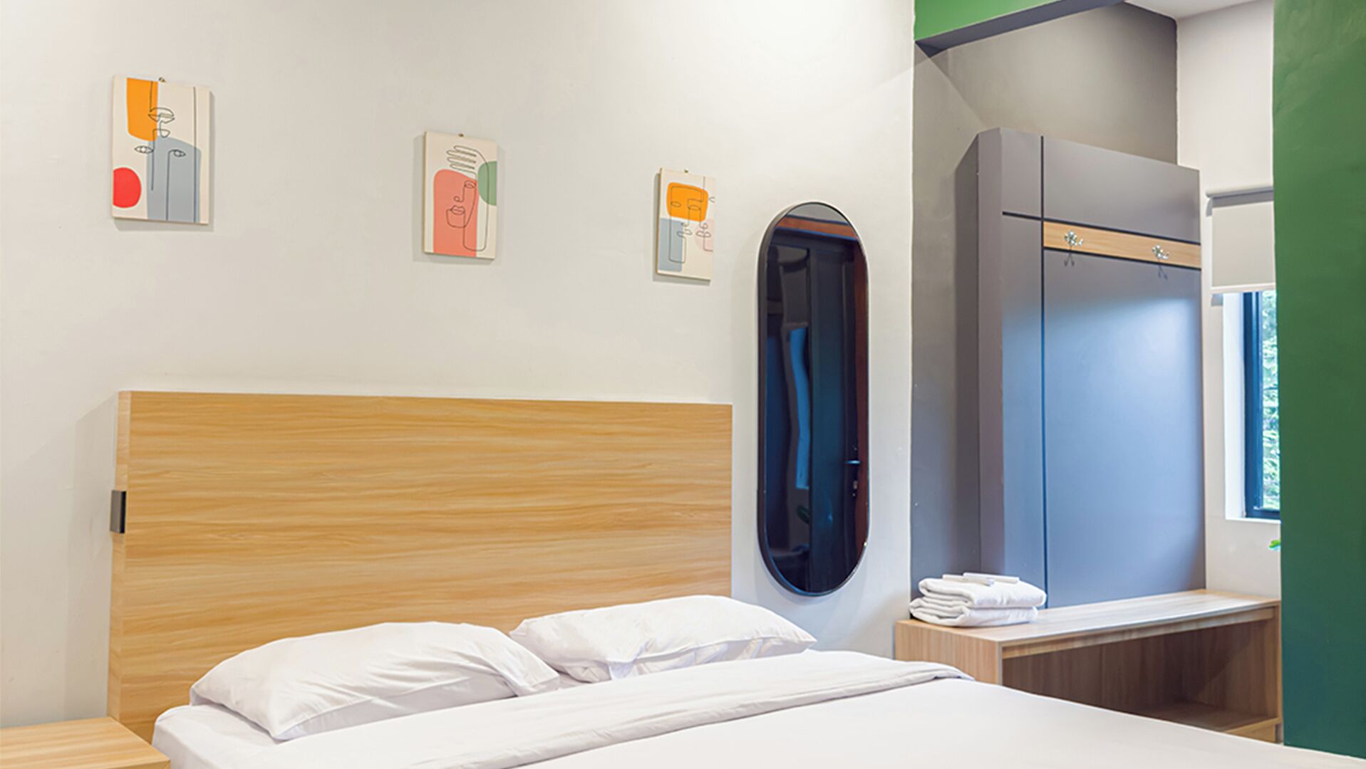 A hotel room with a wooden headboard, a bed with white linens, a wardrobe, and a wall-mounted mirror.
