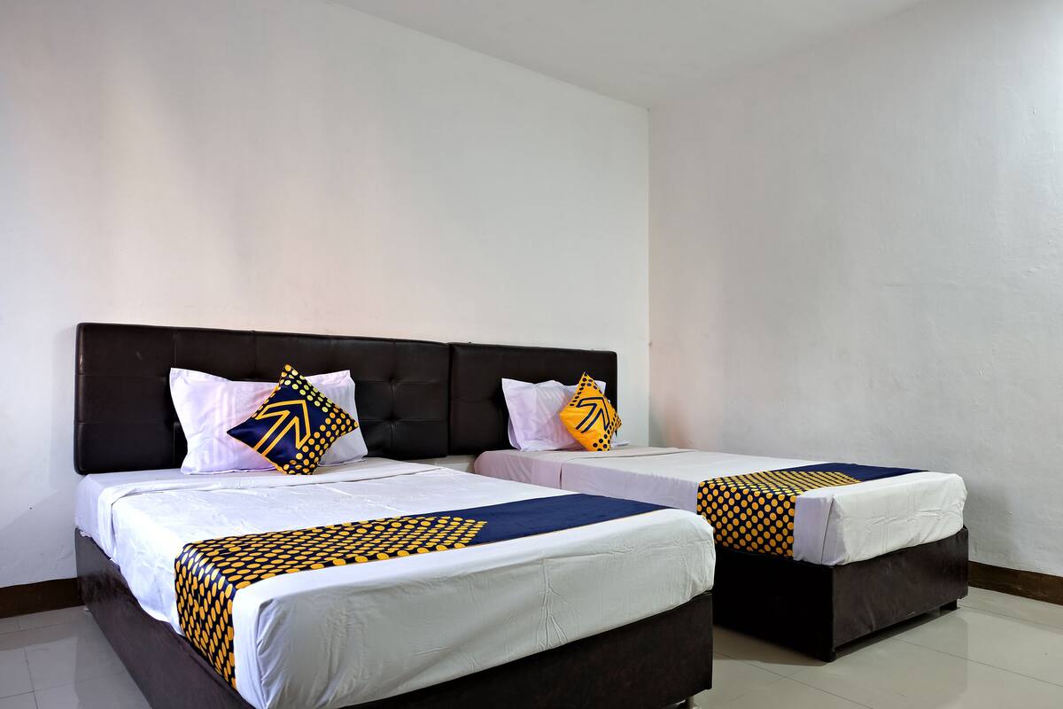 Une chambre d’hôtel avec deux lits, chacun doté d’une tête de lit sombre et de draps blancs.