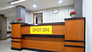 Un mostrador de recepción con un letrero que dice “SPOT ON”, un reloj y dos arreglos florales.