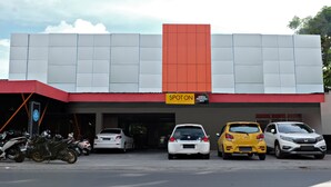 Un edificio con un letrero 'SPOT ON', estacionamiento para coches y motocicletas, y un cielo despejado.
