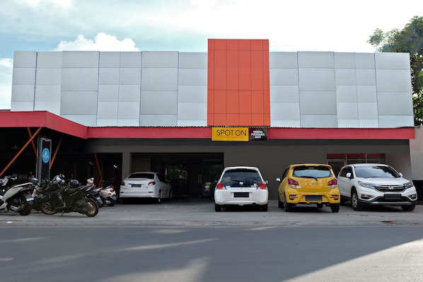 A building with a 'SPOT ON' sign, parking for cars and motorcycles, and a clear sky.