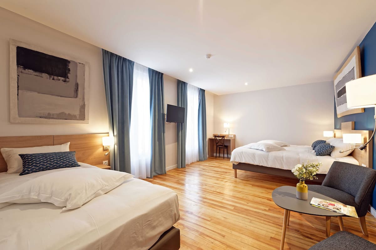 A hotel room with two beds, a desk, a chair, and a small table with a vase and magazine.
