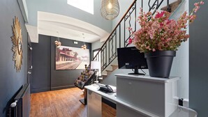 A modern hotel lobby with a wooden floor, a staircase, a black potted plant, a reception desk, and a large framed picture on the wall. - Contact Hôtel de la Gare et son restaurant Côte à Côte (Autun)