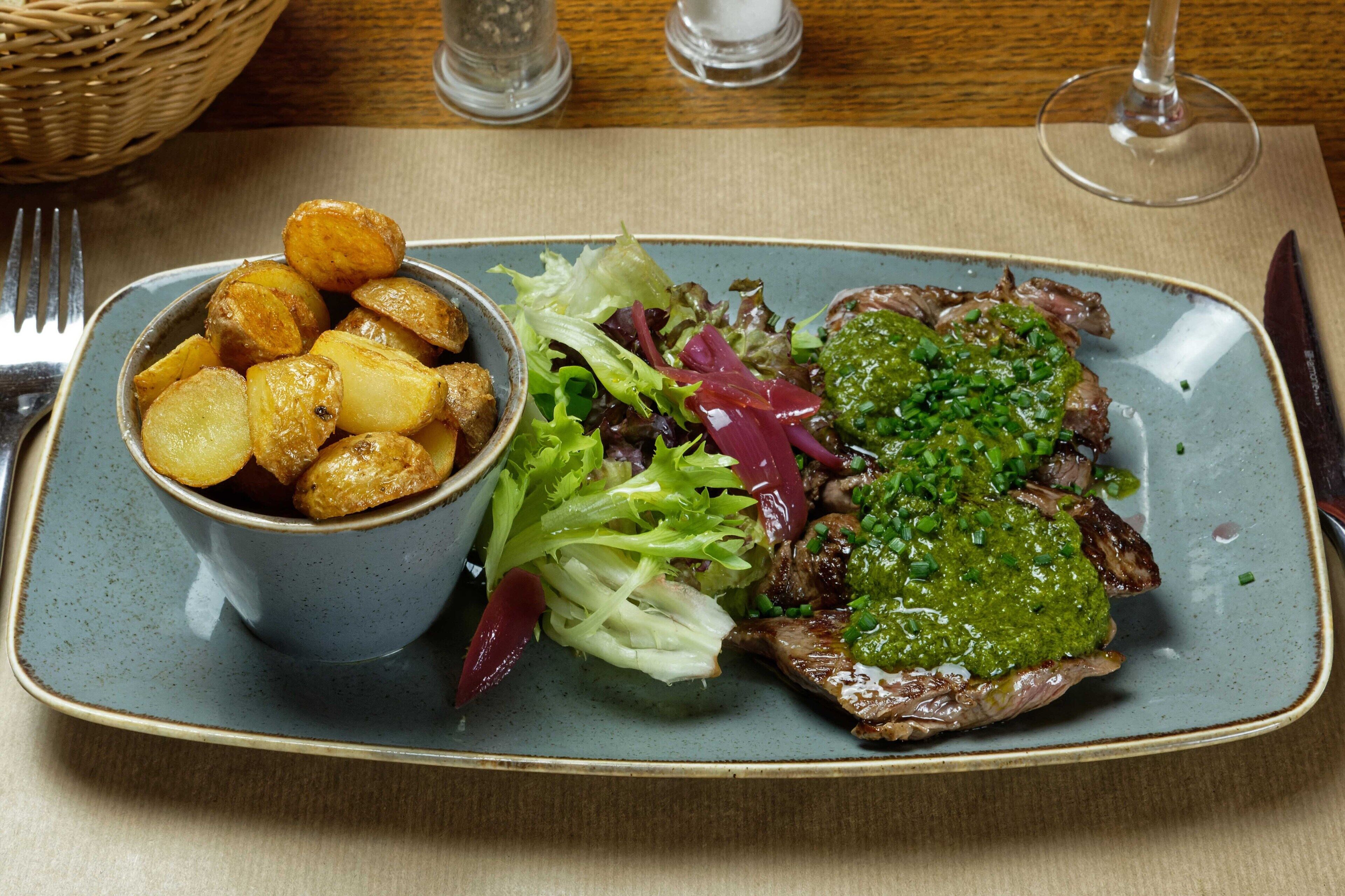 A plate with roasted potatoes, a salad, and a steak topped with green sauce.