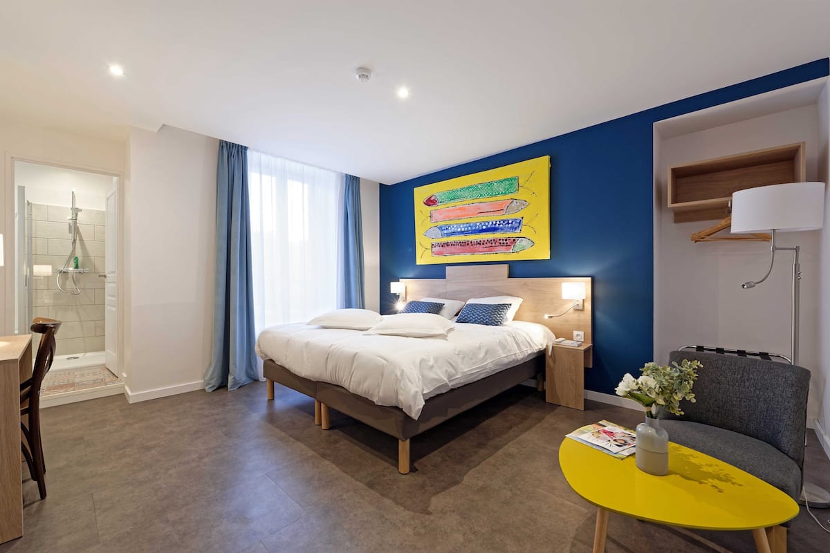 A modern hotel room with a bed, bedside tables, a desk, and a chair.