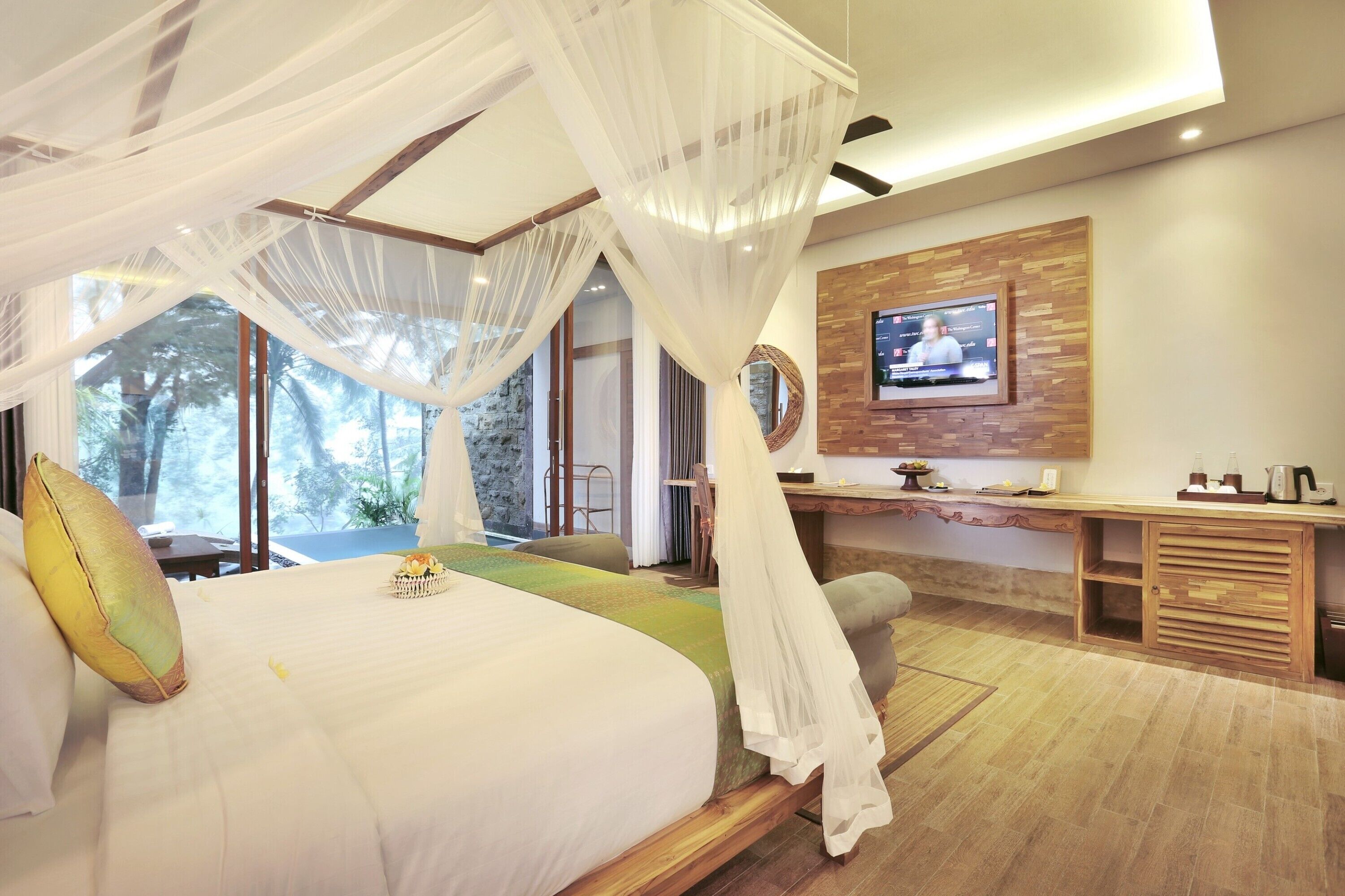 A bedroom with a bed, canopy, TV, and wooden desk.