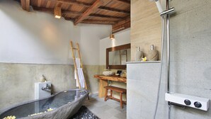 Une salle de bain avec une baignoire en pierre, un banc en bois et une douche dotée d’un panneau de commande.